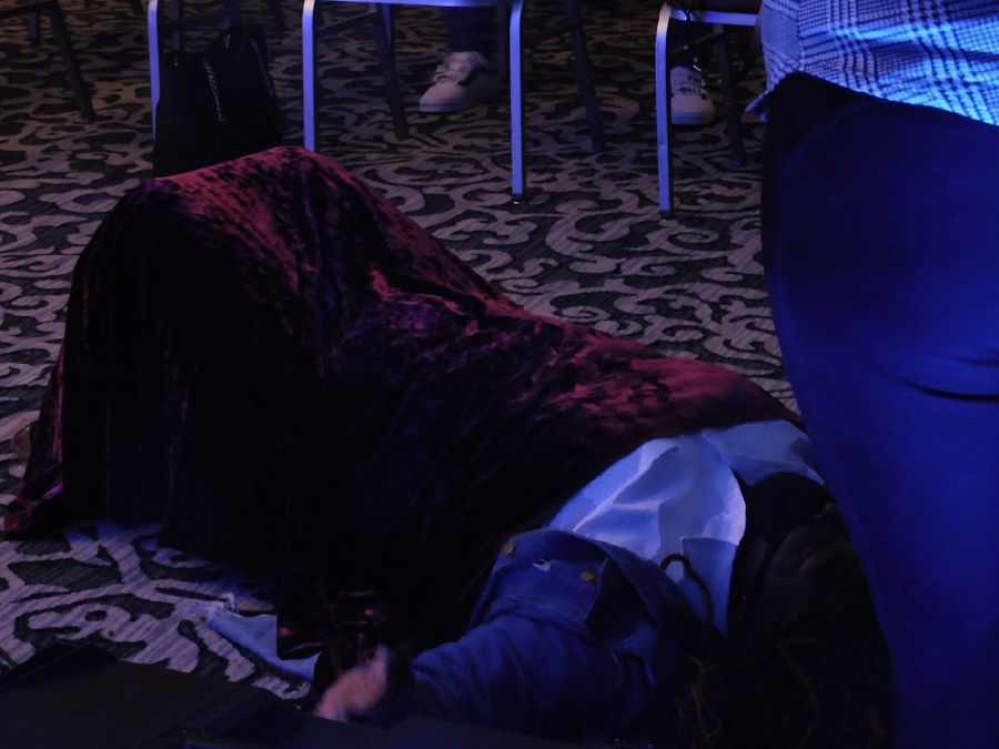 A worshipper lying on the floor under a velvet mantle